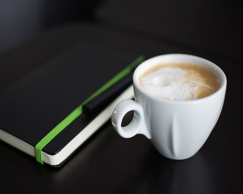 A morning coffee cup on a table next to a notebook